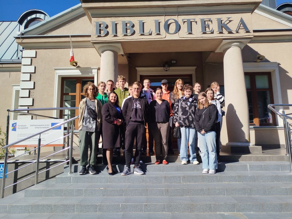 Dyrektor biblioteki Małgorzata Iwańska-Kania oraz młodzież z 1 LO w Sokołowie Podlaskim wraz z opiekunem na schodach przed budynkiem biblioteki.