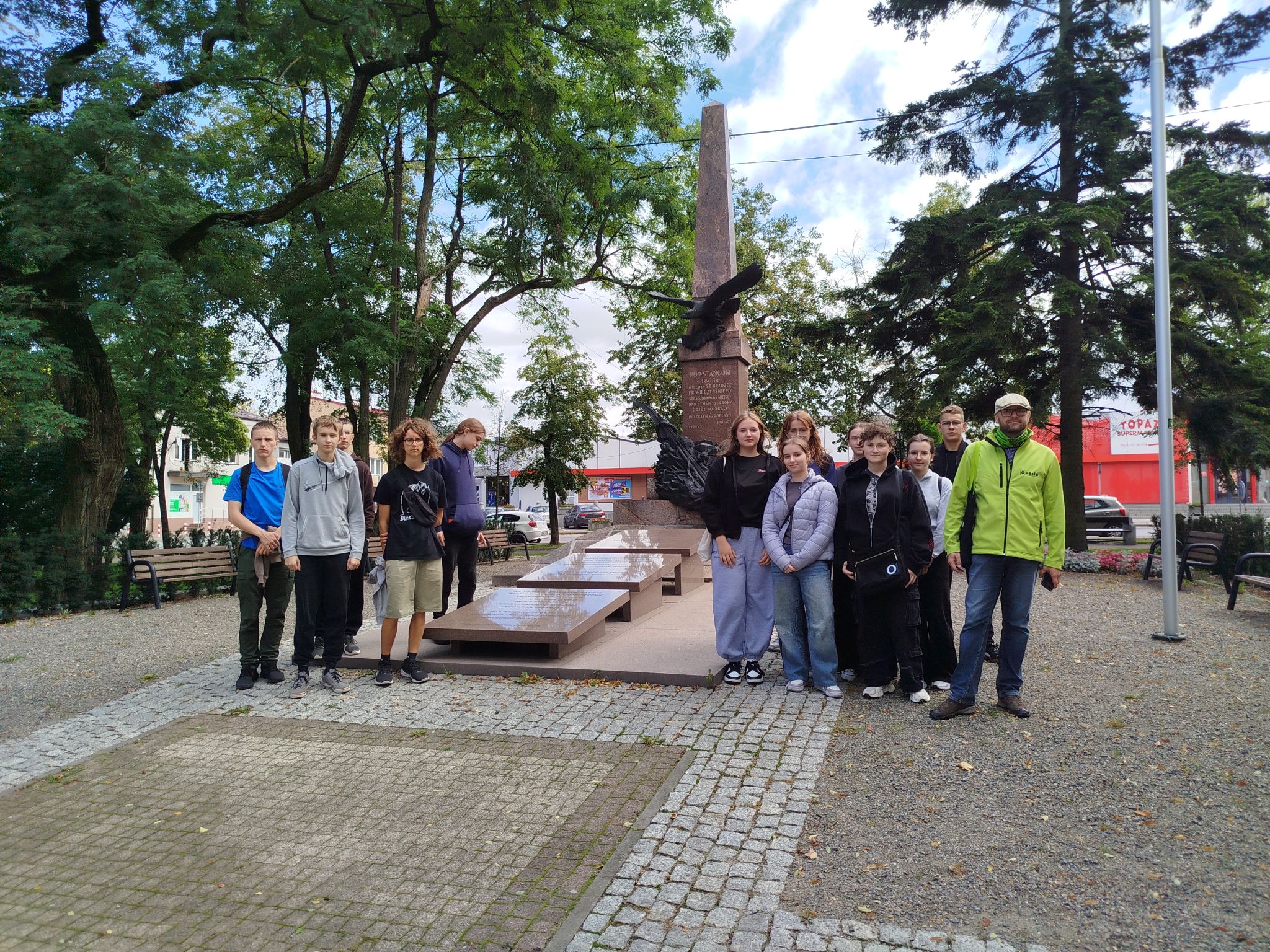 Grupa uczniów i prowadzący stoją przed pomnikiem ks. Brzóski w Sokołowie Podlaskim podczas warsztatów tworzenia Questu.