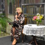Danuta Domańska – zastępca Burmistrza Miasta Sokołów Podlaski siedzi przy stole na którym stoi kolorowy bukiet kwiatów i czyta wiersze Jana Kochanowskiego.