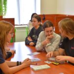 Grupa uczennic siedzi przy stole w bibliotece i pracuje nad materiałami questingowymi.