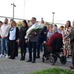 Kilkanaście osób stoi tuż przed złożeniem kwiatów pod pomnikiem. W pierwszym szeregu dyrektor biblioteki Małgorzata Iwańska-Kania oraz pracownicy biblioteki.