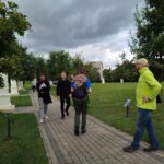 Prowadzący warsztaty questingu idzie alejką w razem z grupą uczniów, w tle widoczne są kapliczki.