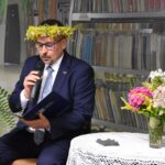 Daniel Krakowski – przewodniczący Rady Miasta Sokołów Podlaski z żółtym wiankiem kwiatów na głowie siedzi przy stoliku i czyta poezję.