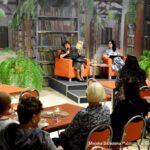 Dyrektor biblioteki Małgorzata Iwańska-Kania oraz Renata Kopczewska podczas spotkania autorskiego w bibliotece. Na pierwszym planie przed paniami siedzi publiczność.