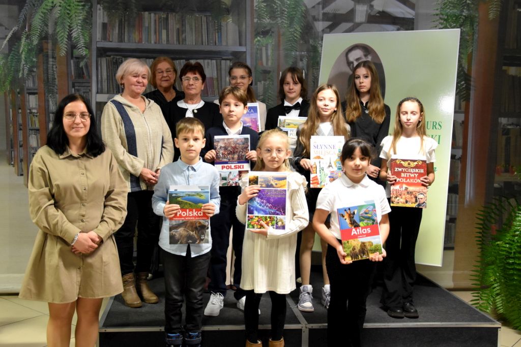 Dziewięcioro dzieci, które zajęły pierwsze trzy miejsca w eliminacjach miejskich konkursu Gałczyńskiego, obok nich stoi trzyosobowa komisja oraz dyrektor biblioteki Małgorzata Iwańska-Kania.