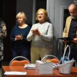 Trzyosobowa komisja - dwie kobiety i mężczyzna. Mężczyzna prezentuje wyniki konkursu. Obok stoi dyrektor biblioteki Małgorzata Iwańska-Kania.