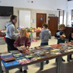 Uczestnicy warsztatów ze smartfonem, wybierają książki potrzebne do pracy.