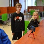 Troje dzieci podczas warsztatów pracuje wspólnie przy projekcie ożywiania drewnianych klocków.