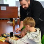 Prowadzący warsztaty pomaga chłopcu ustawić stabilnie telefon między książkami.