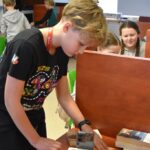 Chłopiec ustawia telefon między książkami podczas warsztatów ze smartfonem w czytelni.