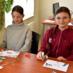 „Dzieci wykonują prace plastyczne przy stole w bibliotece.