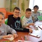 Dzieci przy stole podczas zajęć plastycznych w bibliotece.