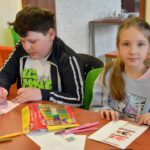 Dzieci wykonują prace plastyczne przy stole w bibliotece.