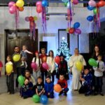 Dzieci i dorośli podczas balu karnawałowego w bibliotece, z kolorowymi balonami.