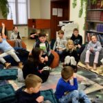 Dzieci siedzą na pufach podczas zajęć w bibliotece.