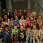 Grupa 22 dzieci (przedszkolaków) siedzi na schodach w trzech rzędach. Za nim szare dwuskrzydłowe drzwi. Dzieci znajdują się w Sokołowskim Ośrodku Kultury.