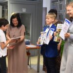 Trójka dzieci podczas odbierania nagród książkowych i dyplomów. Dzieci odbierają nagrody od dyrektor biblioteki Małgorzaty Iwańskiej-Kania. Z tyłu stoją trzy kobiety z komisji konkursowej.