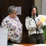 Dyrektor Biblioteki Małgorzata Iwańska-Kania prezentuje książkę kulinarną „Z miłości do tradycji. Smaki Ziemi Siedleckiej” podczas Festiwalu Literatury Kulinarnej. Obok niej stoi Teresa Nazarczuk. Na stole znajduje się tablica z opisem zalewajki – potrawy wspominanej w filmie 'Jak rozpętałem II wojnę światową'.
