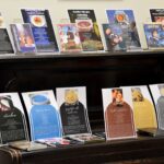 Czarne pianino, na którym ustawiono i położono pudełka z płytami DVD z filmami i bajkami, w których znajdują się przepisy kulinarne. Obok pudełek umieszczono kartki z wydrukowanymi przepisami z tych filmów. Wydrukowane przepisu są stylizowane na wór okładek z tych filmów.
