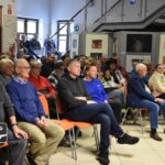 Pobliczność podczas spotkania na Festiwalu Literatury Kulinarnej siedzi na krzesłach na holu biblioteki.