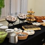 Stół z regionalnymi przysmakami podczas Festiwalu Literatury Kulinarnej w sokołowskiej Bibliotece. Na czarnym obrusie ustawiono m.in. sałatki z marchwi i kapusty, pączki, ciasta z czekoladą i jabłkami, eklerki, roladki oraz ciasteczka 'Sokołek' z cukrowym herbem. Wszystko przygotowane do degustacji dla uczestników wydarzenia.