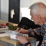 Autor Andrzej Ziemiański podpisuje książkę, obok leży czerwona róża i kilka książek.