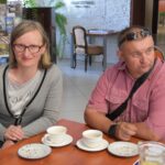 Kobieta w okularach i mężczyzna w różowej koszuli siedzą przy stole z pustymi filiżankami i talerzami po cieście.