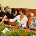 Uczestnicy warsztatów w bibliotece przygotowują kadzidła słowiańskie z ziół, rozmawiając i uśmiechając się.