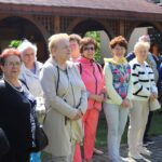 Grupa seniorów stojąca na zewnątrz podczas wycieczki, w słoneczny dzień.