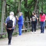 Cztery kobiety spacerują alejką obok krzyży w lesie, oglądając i fotografując miejsce pamięci.
