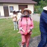 Uśmiechnięta seniorka w stroju pszczelarskim na tle pasieki.