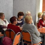 Słuchacze podczas spotkania z Katarzyną Nowosielską siedzą przy stolikach. Na stolikach filiżanki na spodkach oraz wysokie szklanki z wodą.