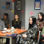 Publiczność podczas spotkania w bibliotece siedzi przy stolikach. Jedna z osób to dyrektor biblioteki Małgorzata Iwańska-Kania.