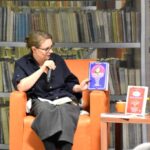 Dorota Filipiak trzyma w ręku jedną z książek Michała Skoczka i prezentuje ją publiczności.