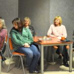 Publiczność podczas spotkania siedzi przy stolikach z kawą i herbatą w filiżankach.