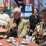 Wacław Kruszewski siedzi na środku sali i przemawia do mikrofonu.
