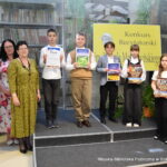 Pięcioro dzieci ze starszej grupy wiekowej - zwycięzców pozuje z dyplomami i nagrodami za konkurs. Obok nich stoi komisja oraz pani dyrektor biblioteki Małgorzata Iwańska-Kania.