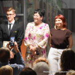 Wiesława Kwiek pozuje do wspólnego zdjęcia z młodym akordeonistą oraz Liwią Długosz. Na pierwszym planie uczestnik fotografuje ich telefonem komórkowym.